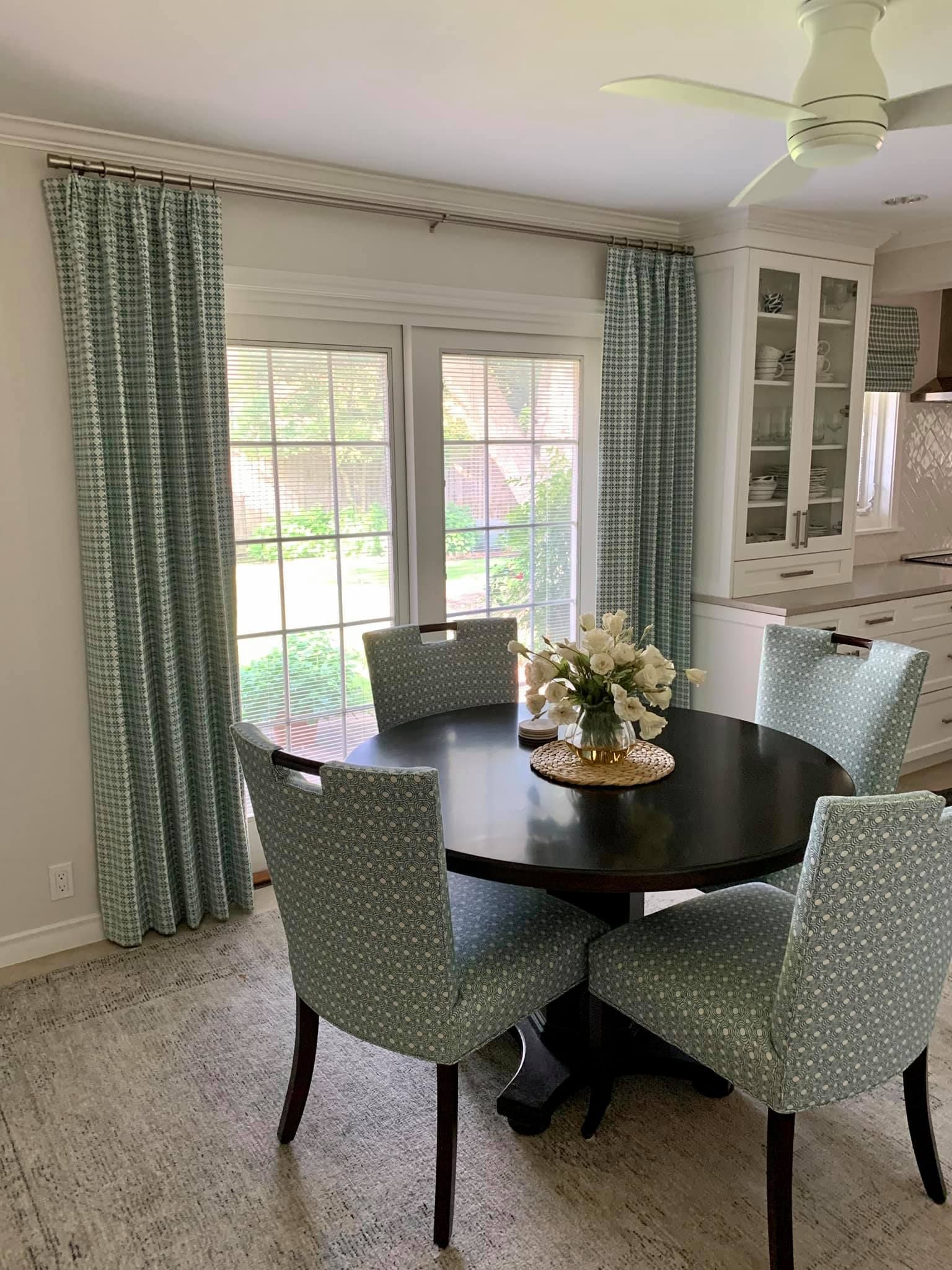 Dining room with round table, four patterned chairs, and patterned curtains.