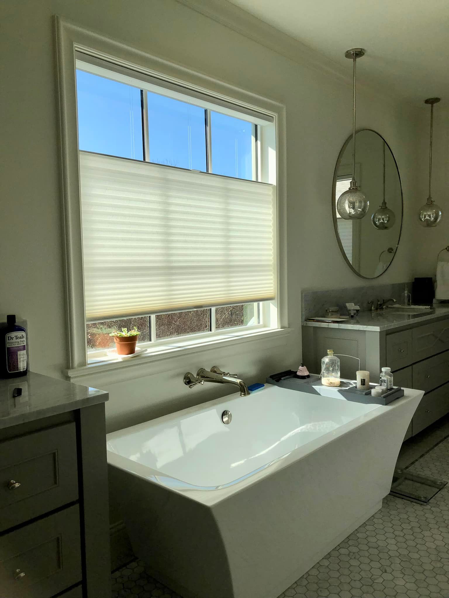 Bathroom with a white bathtub, window with blinds, and pendant lights.