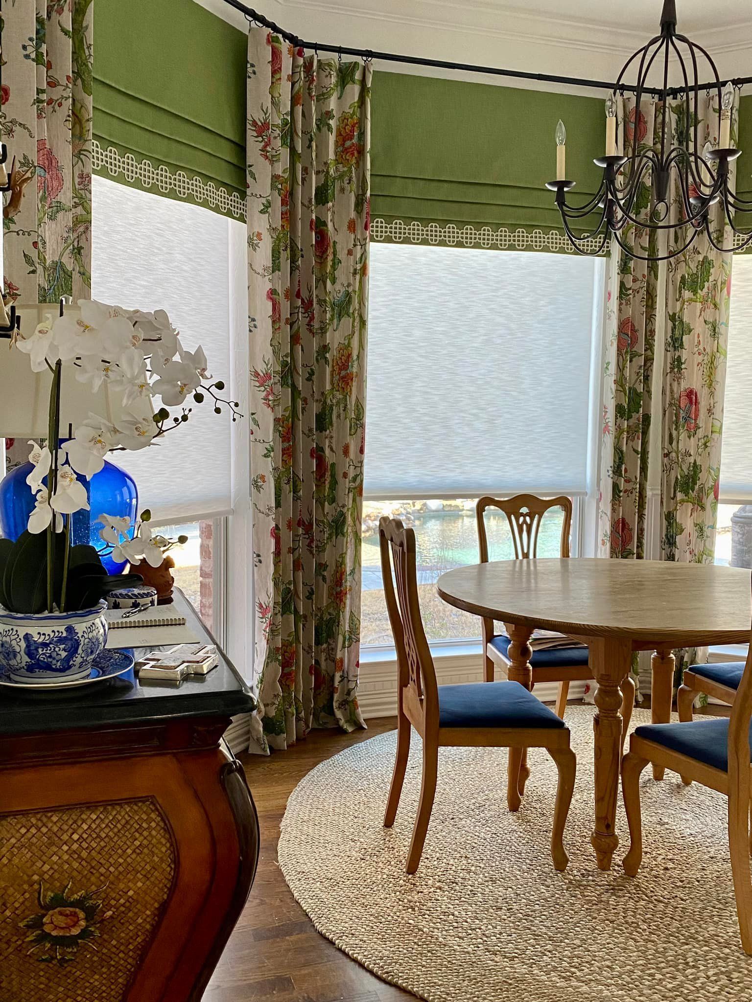 Dining room with floral curtains, round table, chandelier, and a rug.