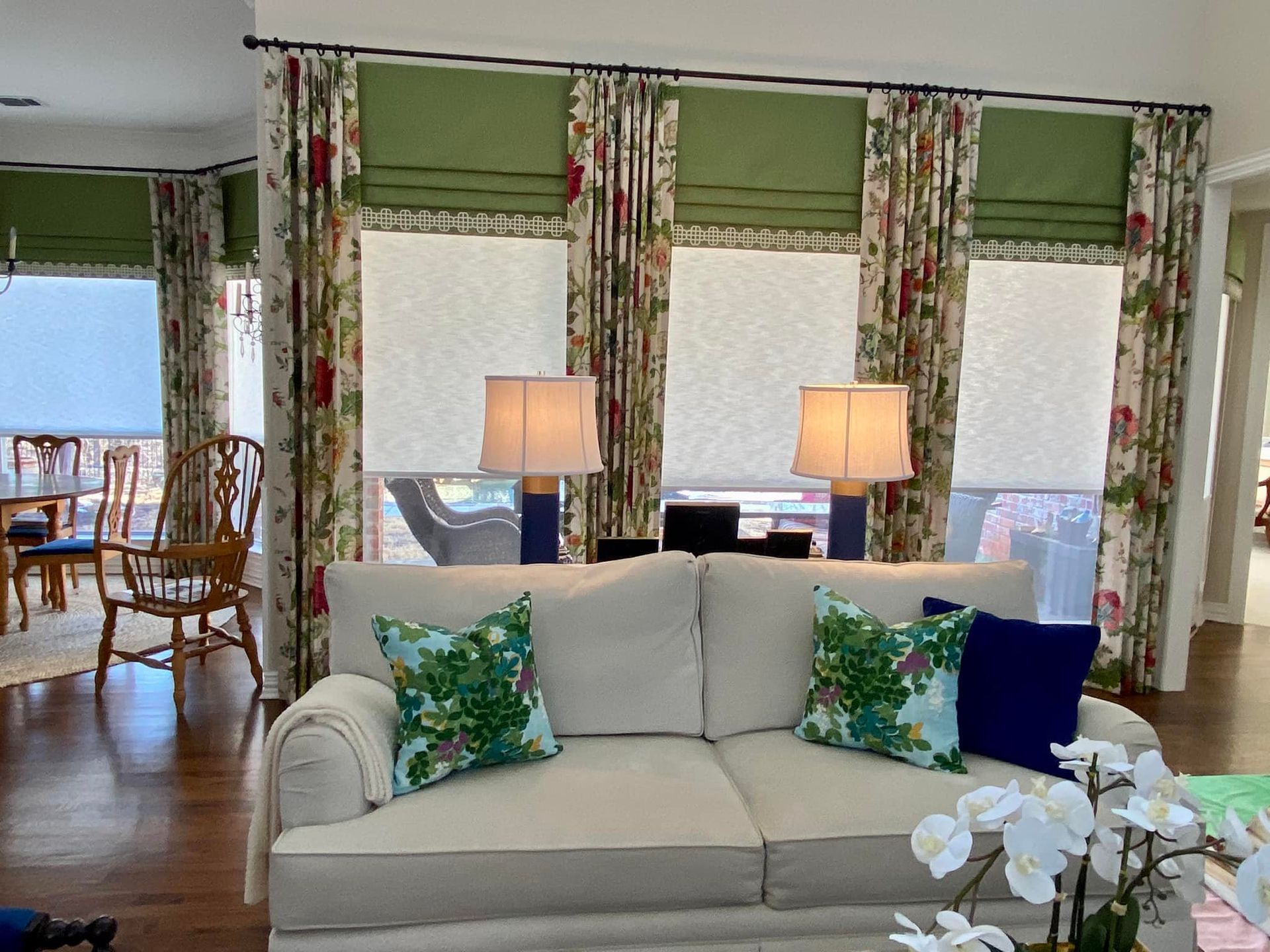 Living room with a white sofa, lamps, floral curtains, and green Roman shades.