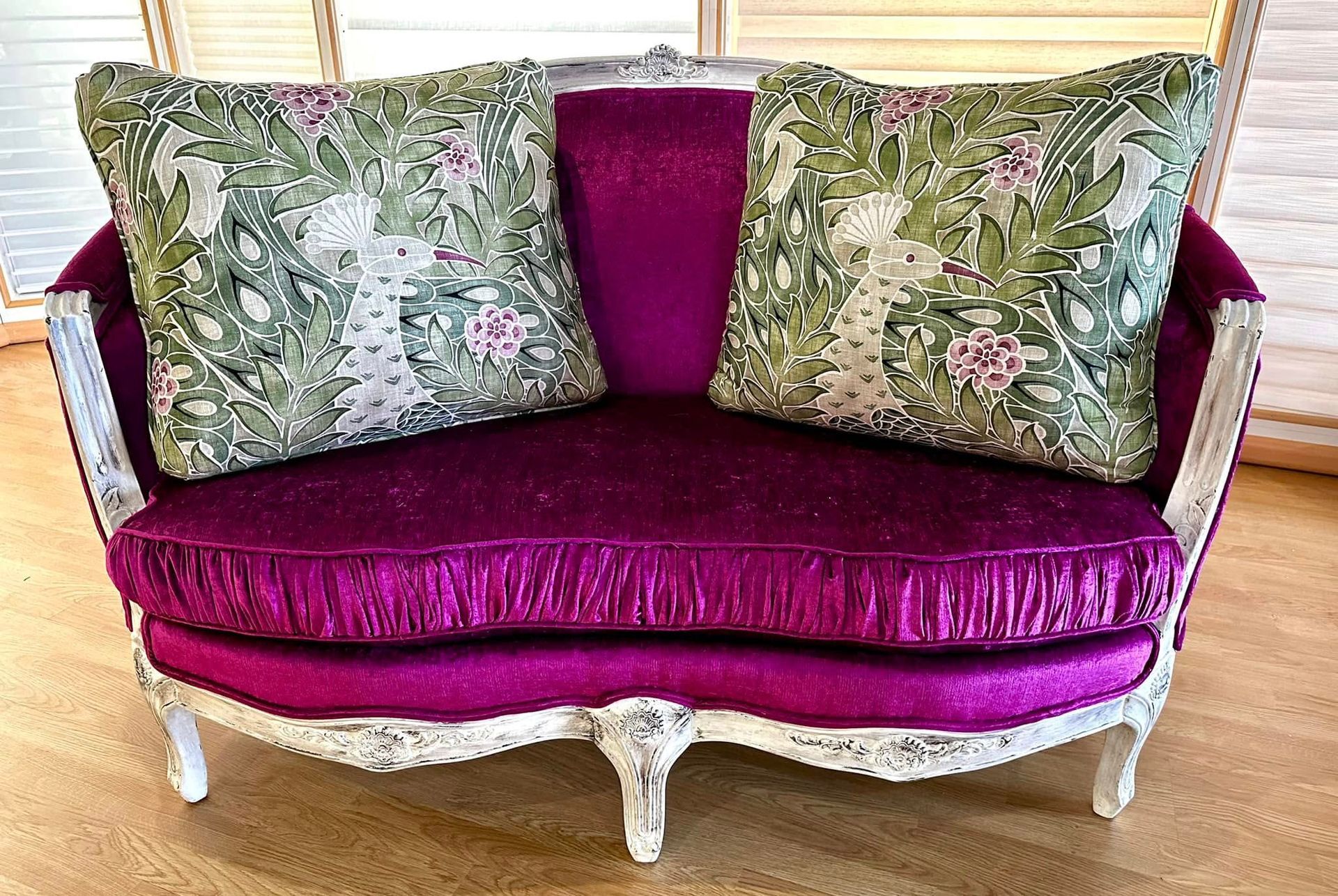 Purple velvet loveseat with two decorative floral pillows, white carved frame.