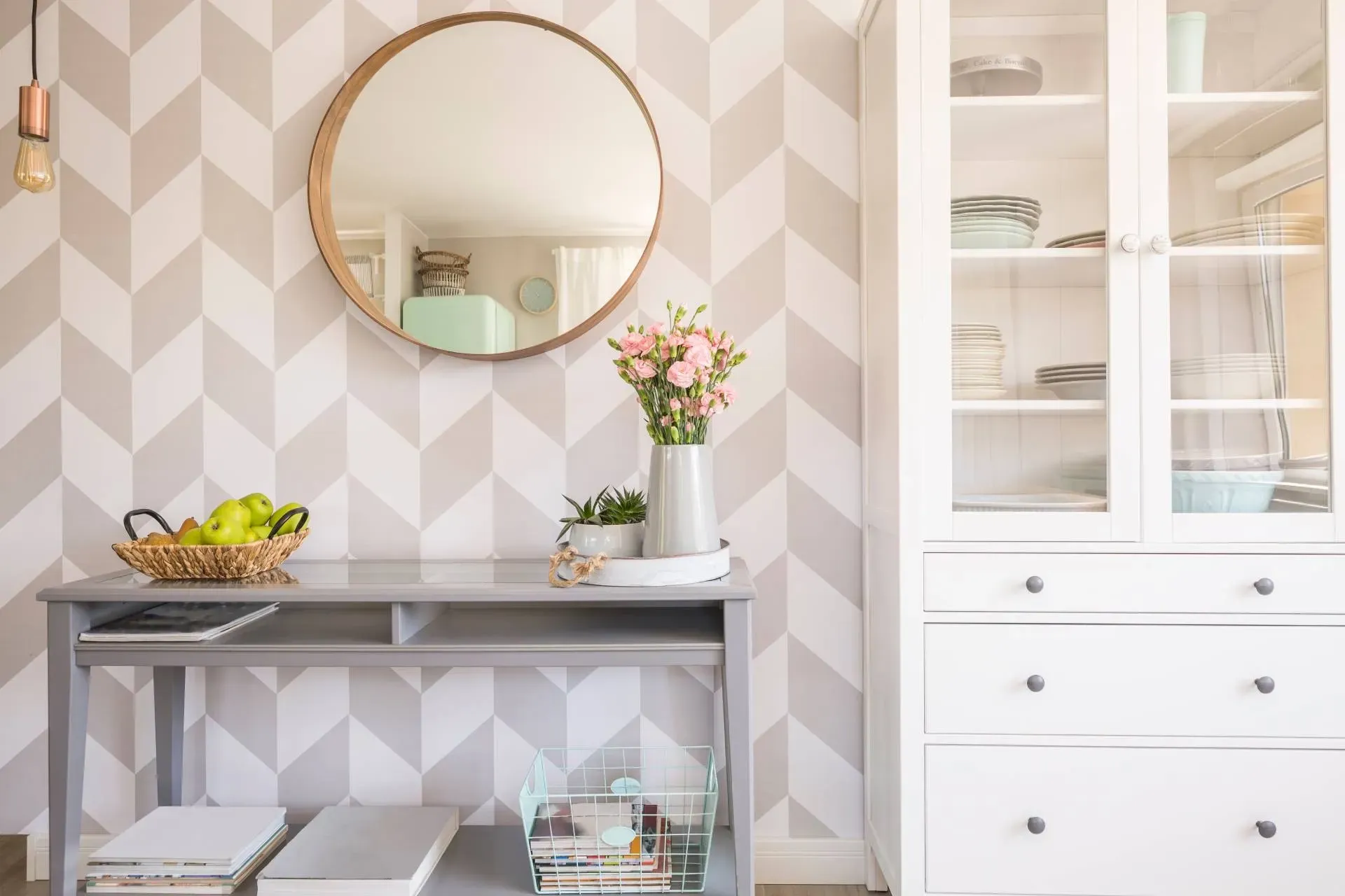 Gray and white patterned wall with a round mirror, desk, and white cabinet.