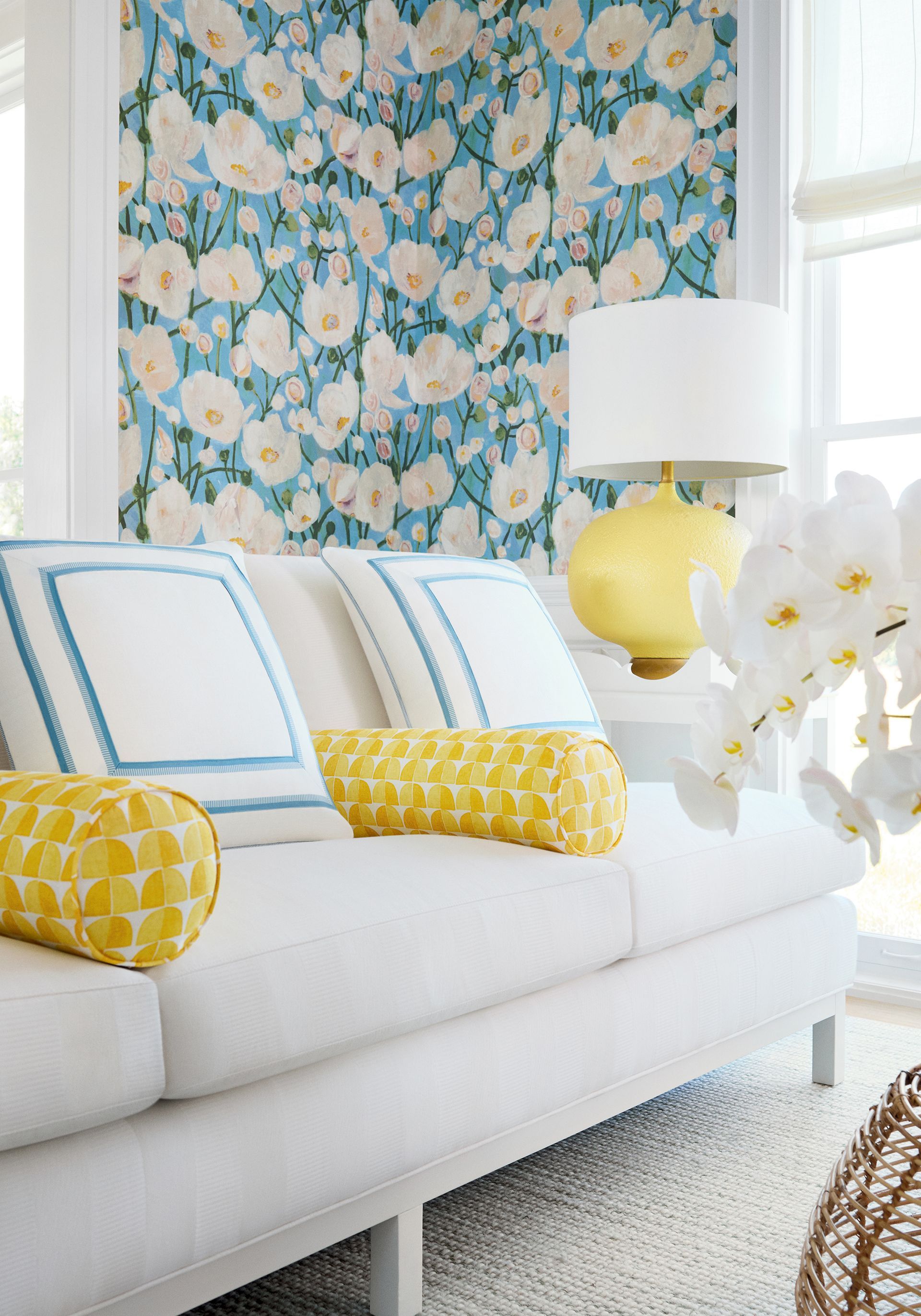 White sofa with blue and yellow accents in front of floral wallpaper.
