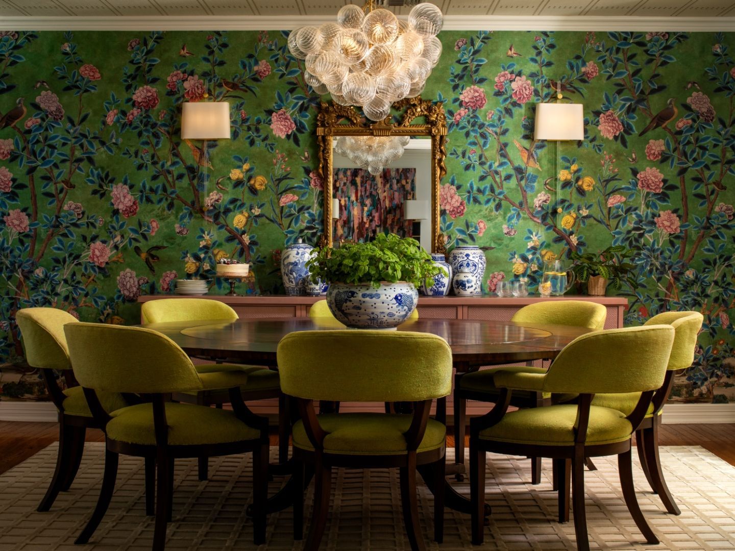 Dining room with floral wallpaper, round table, lime green chairs, and ornate chandelier.