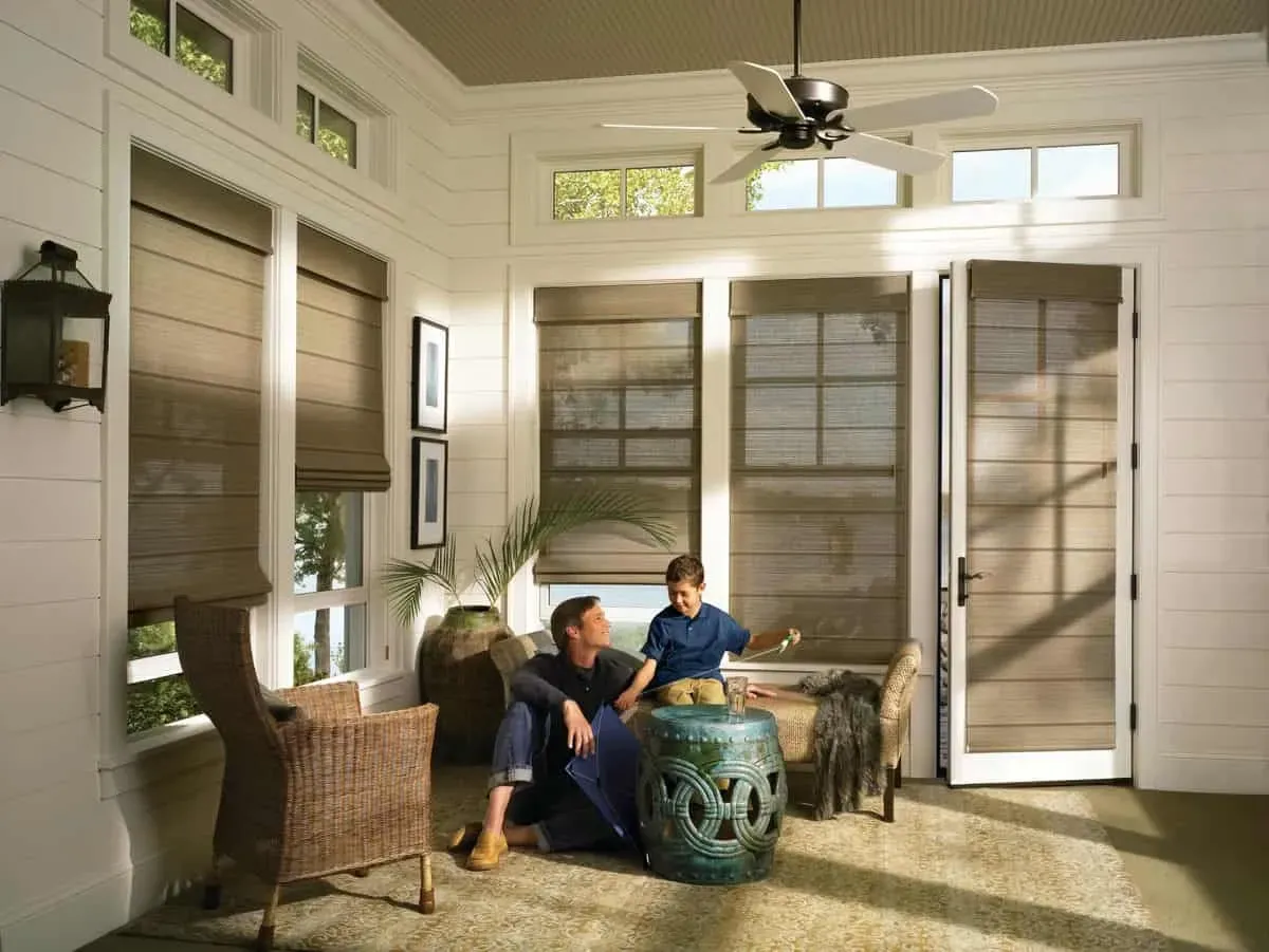 Man and child in sunroom with blinds and a fan.