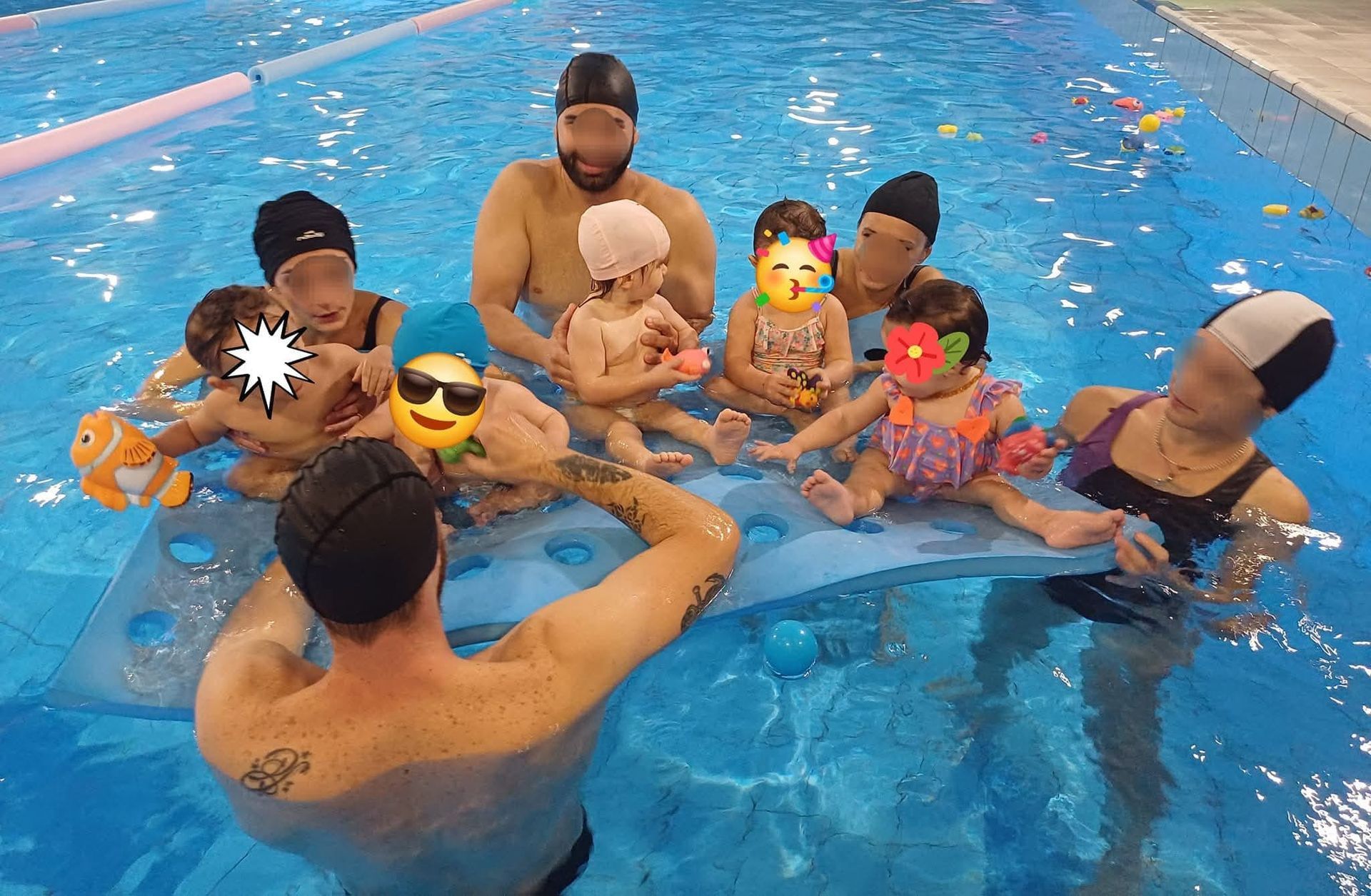 Un istruttore di nuoto e diversi bambini in piscina su un materassino galleggiante; giornata di sole.