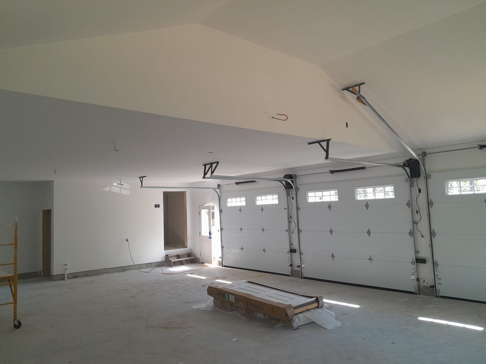 Spacious, empty garage with white walls, doors, and ceiling. Ajar garage doors. Light shines through.