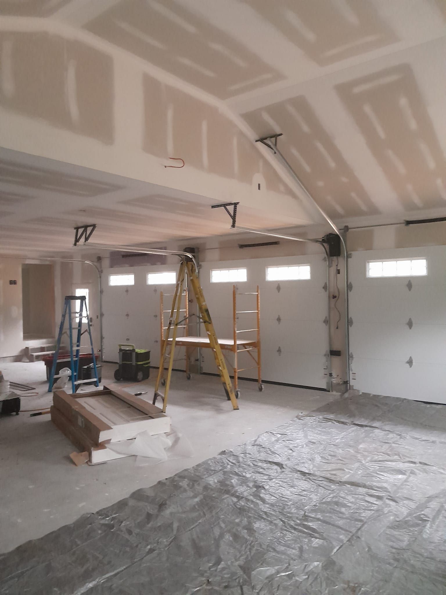 Construction site: unfinished garage with drywall, ladder, scaffolding, and concrete floor.