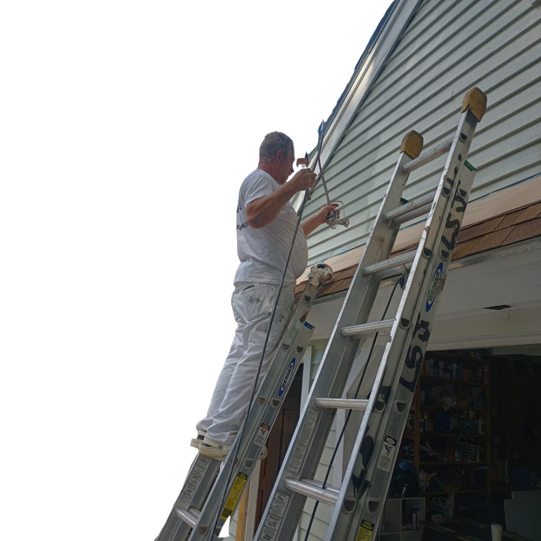 Person painting siding, using a spray gun, standing on a leaning ladder, next to a building.