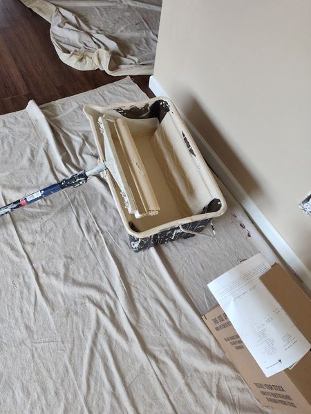Paint roller tray with roller, on drop cloth, near wall.