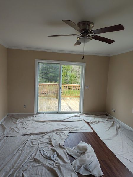 Room with beige walls, a sliding glass door to a deck, and paint tarps covering the floor.