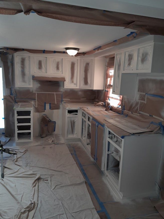 Kitchen being painted, cabinets and countertops masked with brown paper and blue tape.