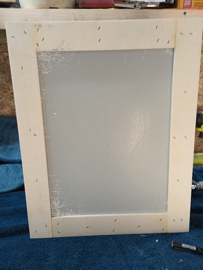 Wooden cabinet door with frosted glass panel, fastened with small nails.