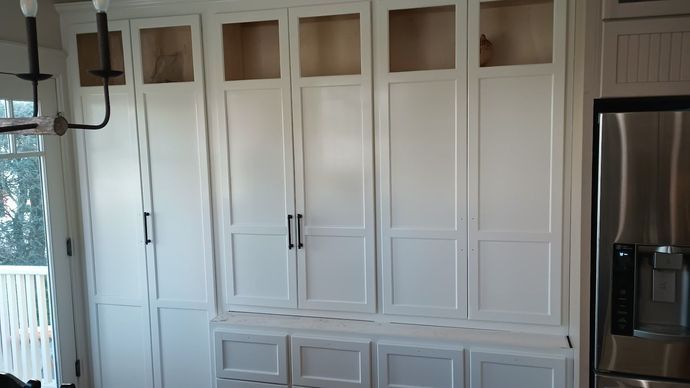 White kitchen cabinets with black handles and stainless steel refrigerator.
