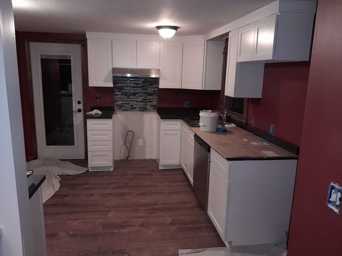 Kitchen with white cabinets, dark countertops, dark backsplash, and red walls.