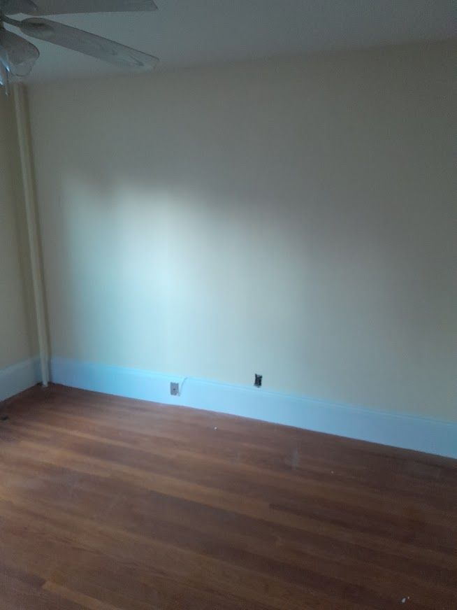 Empty room with hardwood floors, beige walls, and light blue baseboard.