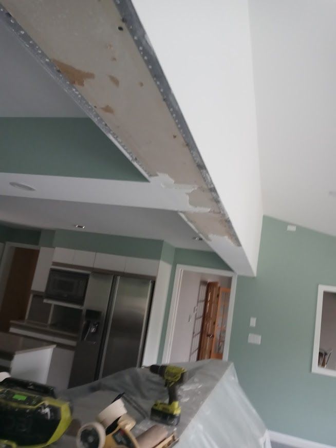 Construction site with exposed ceiling framing, drywall, tools, and painted walls in shades of white and green.