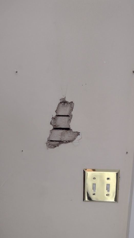 Hole in a wall with exposed internal structure and a nearby electrical outlet.