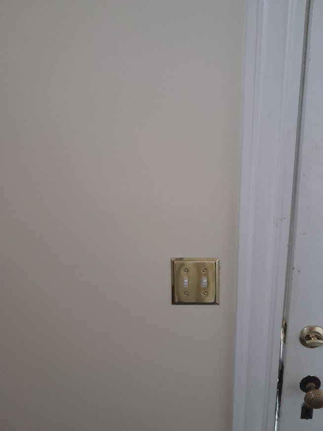 Wall with two light switches, beige paint, and door on right. Gold switch plate.