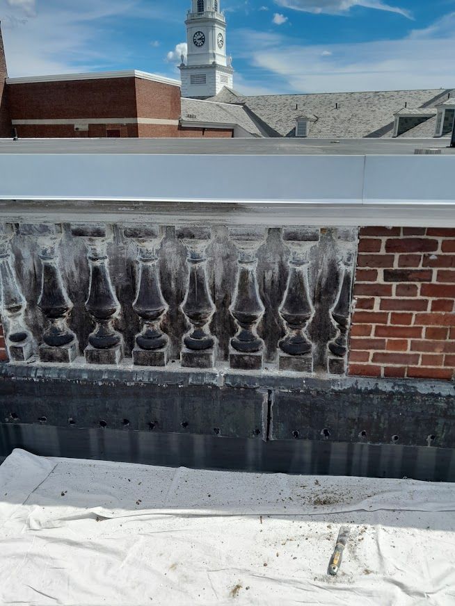 Stone balustrade with brick wall, topped with white trim, building and clock tower in the background.