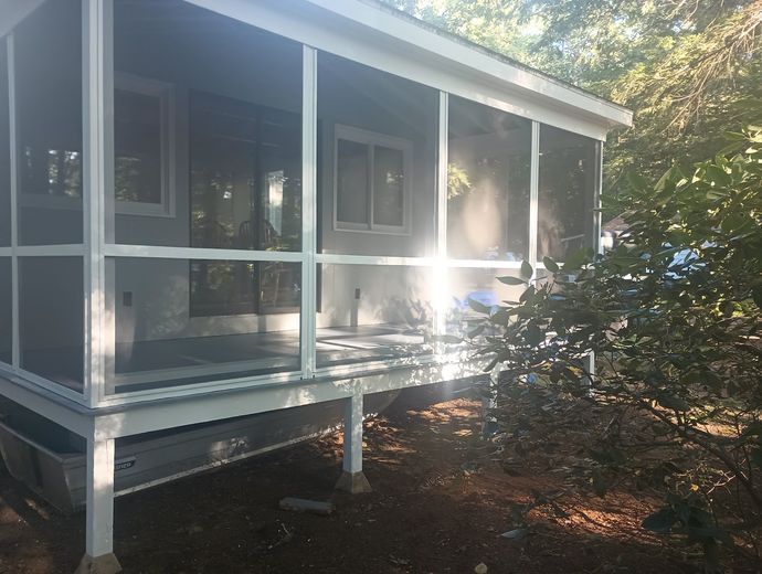 Screened-in porch on a raised deck with white trim and gray walls; surrounded by trees.