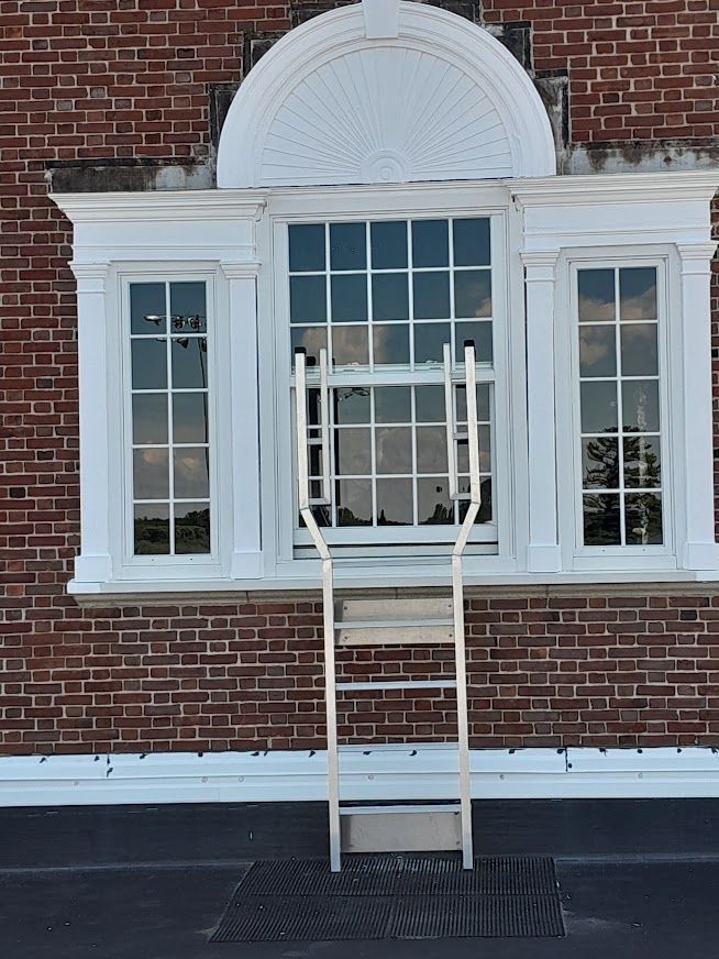White ladder extends from a rooftop to a window in a brick building.