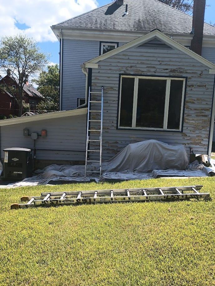 House with peeling paint, ladder propped against the side, and another ladder on the grass.