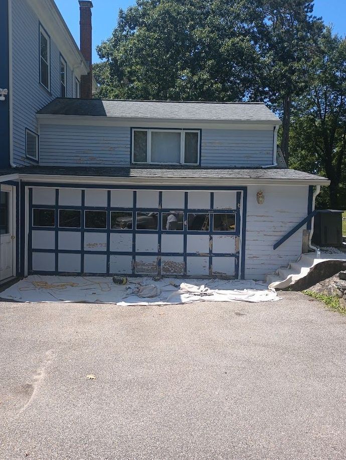 Blue and white house with garage, asphalt driveway, and trees.