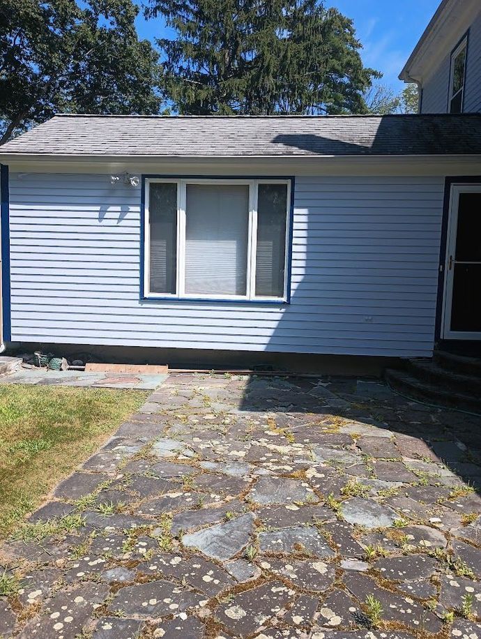 Light blue building with a window, dark blue trim, and stone patio.