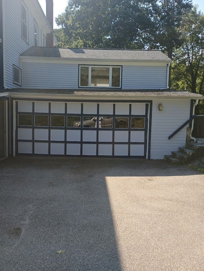 Garage with light blue siding and a multi-pane glass door, located near a house with trees in the background.