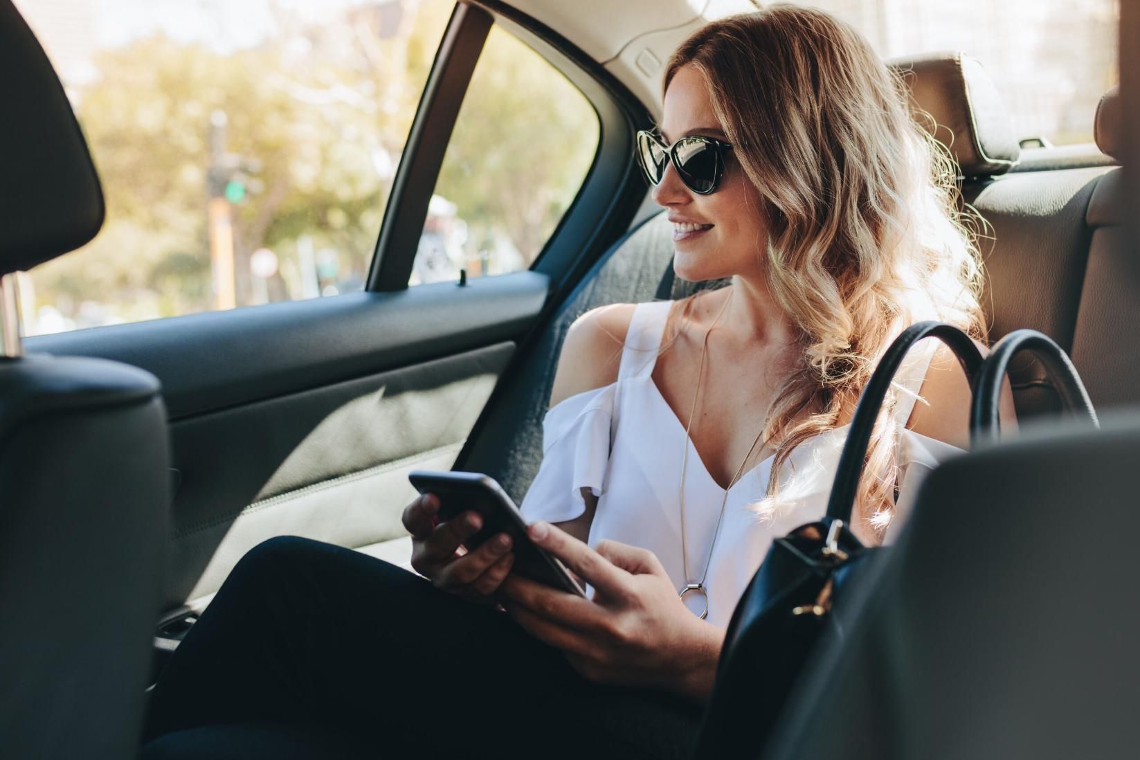 A Woman Is Sitting in The Back Seat of A Car Looking at Her Cell Phone — Greenaway's Taxi in Lansdowne, NSW