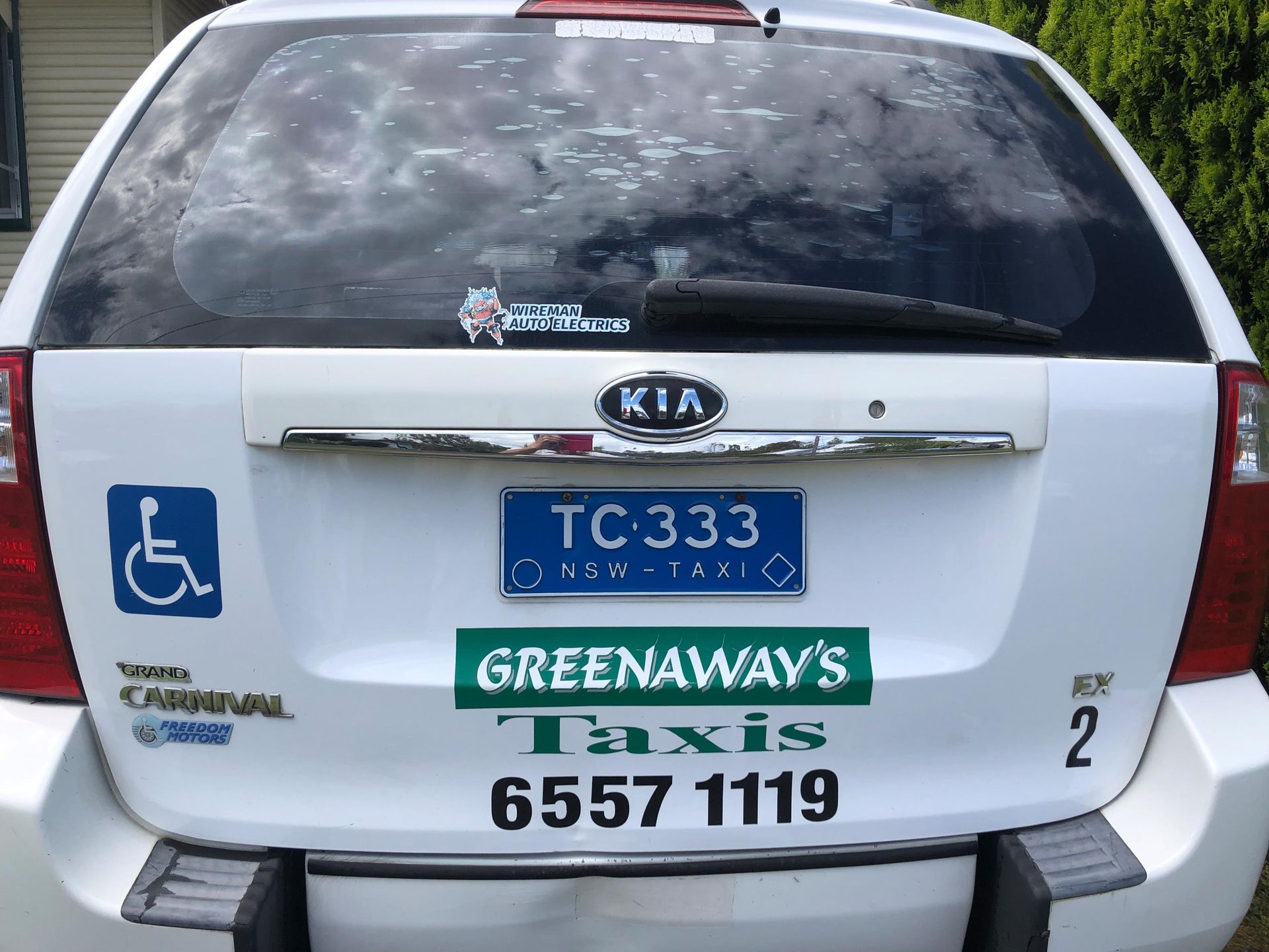 Back of a white Kia Carnival taxi with a disabled access sticker, license plate TC-333, and Greenaway's Taxis logo — Greenaway's Taxi in Wingham, NSW