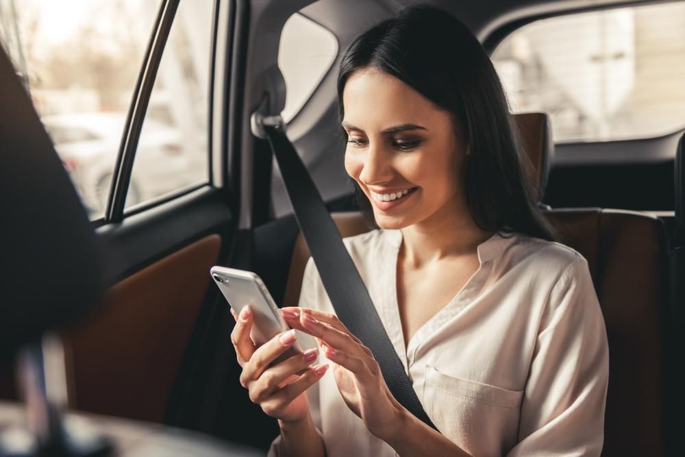 A Woman Is Sitting in The Back Seat of A Car Looking at Her Cell Phone — Greenaway's Taxi in Krambach, NSW
