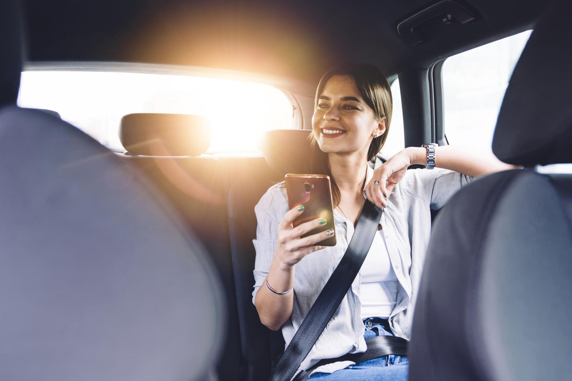 A Woman Is Sitting in The Back Seat of A Car Looking at Her Phone — Greenaway's Taxi in Elands, NSW