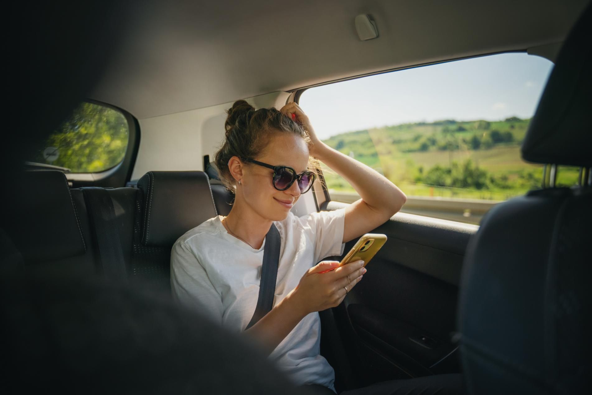 A Woman Is Sitting in The Back Seat of A Car Looking at Her Phone — Greenaway's Taxi in Tinonee, NSW