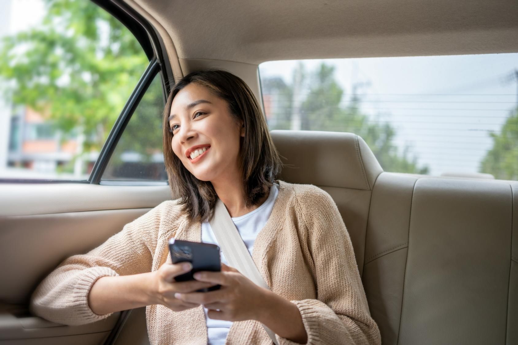A Woman Is Sitting in The Back Seat of A Car Using Her Cell Phone — Greenaway's Taxi in Krambach, NSW