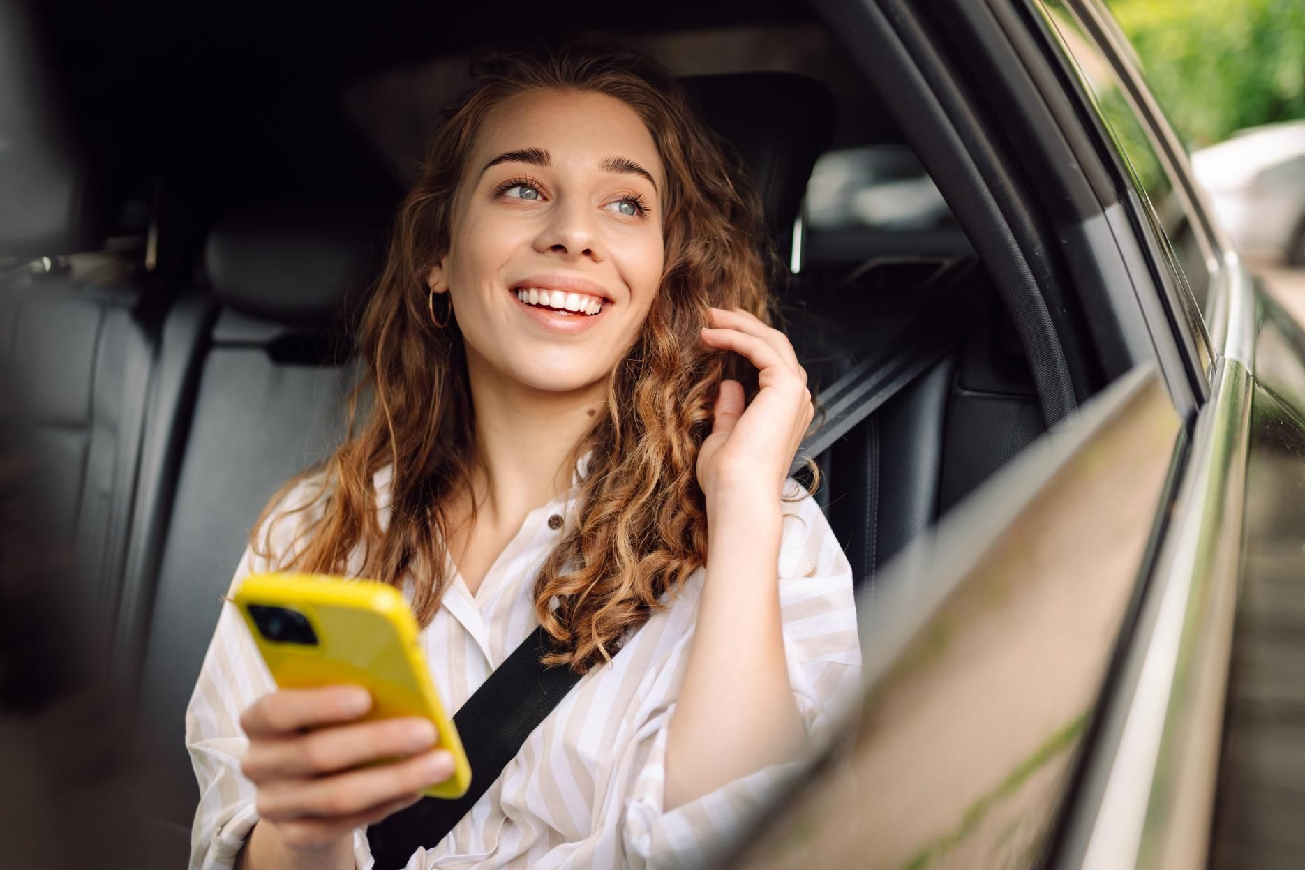 Woman with curly hair smiles in a car, holding a yellow phone — Greenaway's Taxi in Lansdowne, NSW