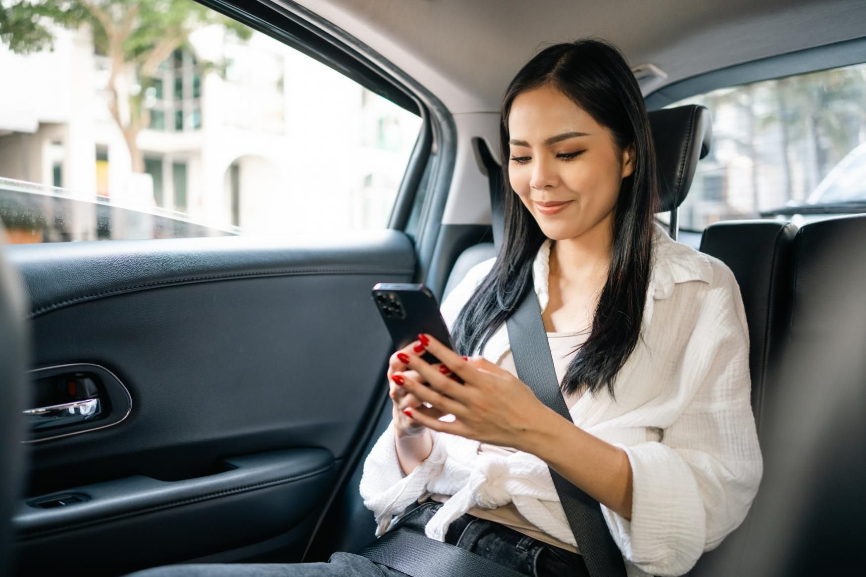 A Woman Is Sitting in The Back Seat of A Car Looking at Her Cell Phone — Greenaway's Taxi in Harrington, NSW