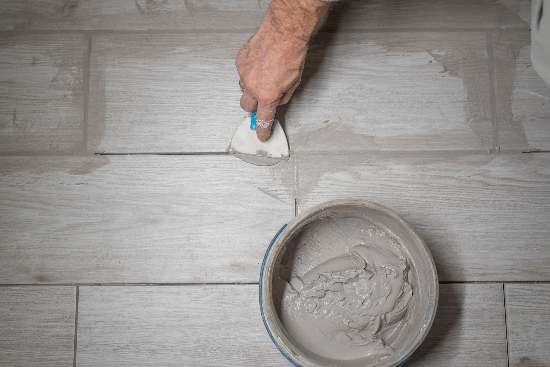 A person is applying grout to a tile floor with a spatula.
