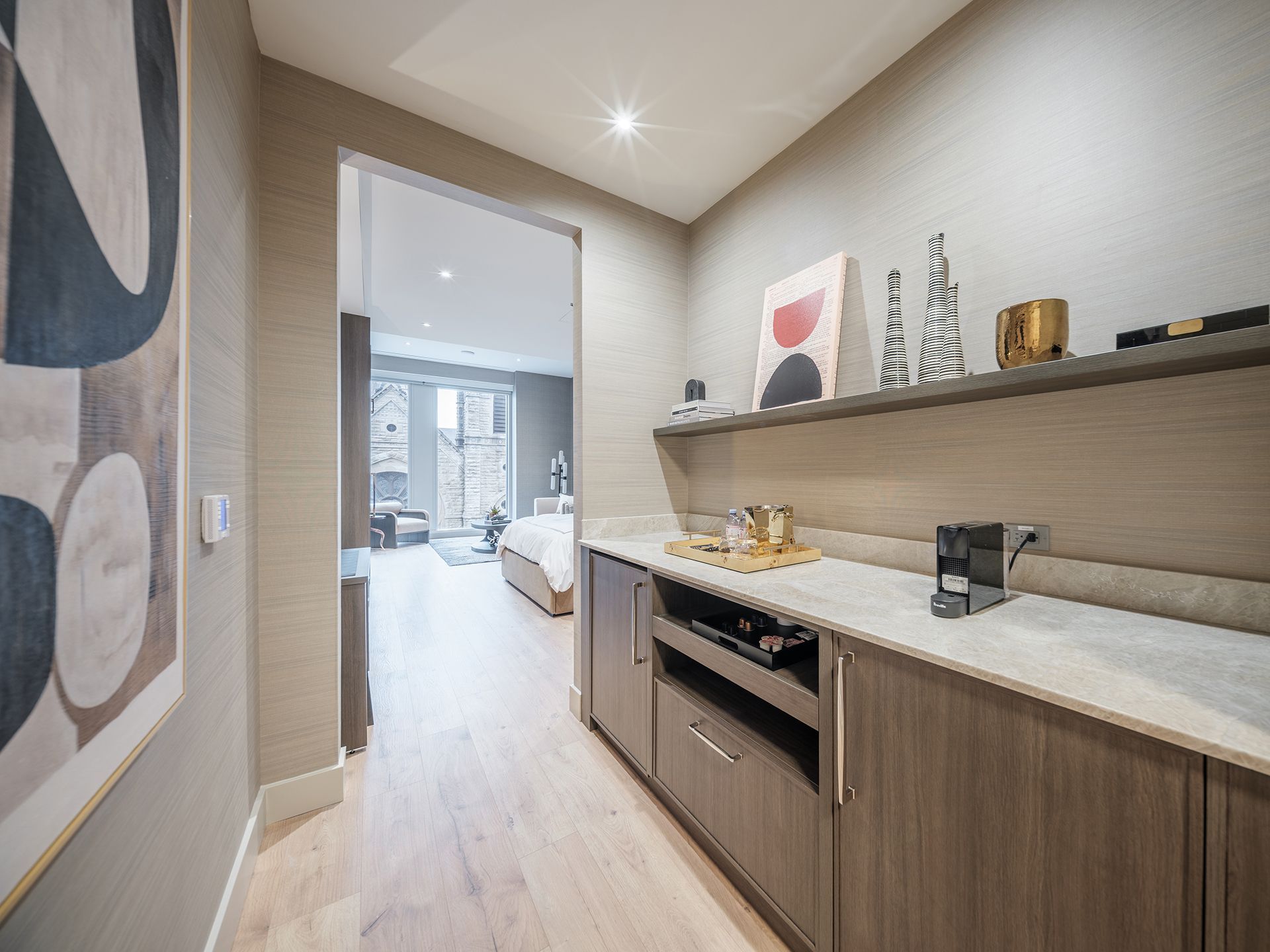A hallway in a house with a kitchen and a painting on the wall.