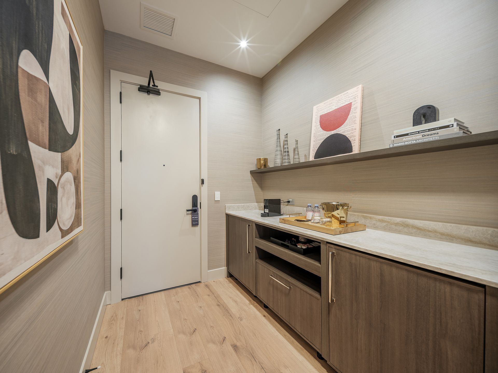 A hallway with a door , cabinets , a shelf and a painting on the wall.