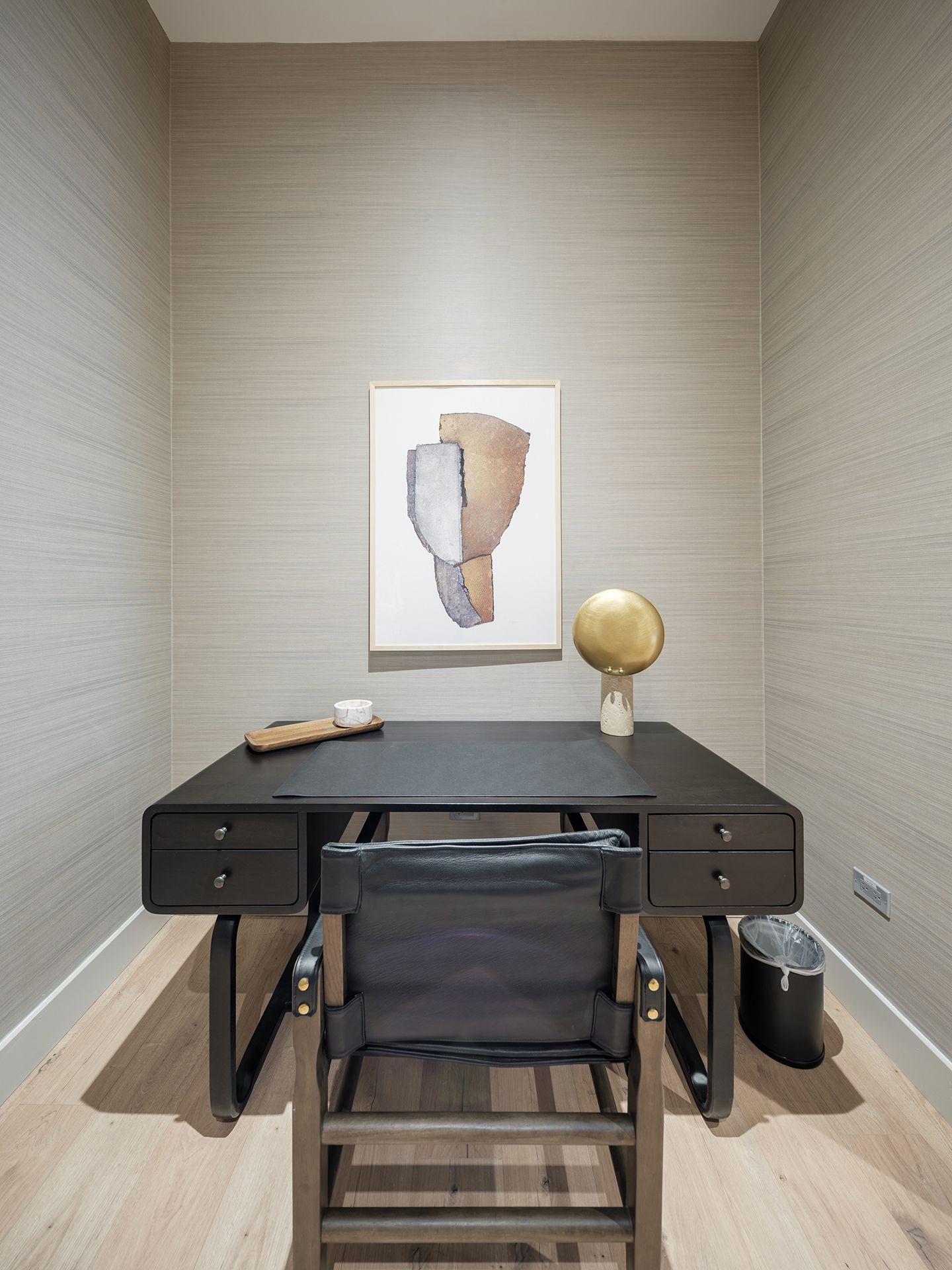 A small office with a desk , chair and painting on the wall.