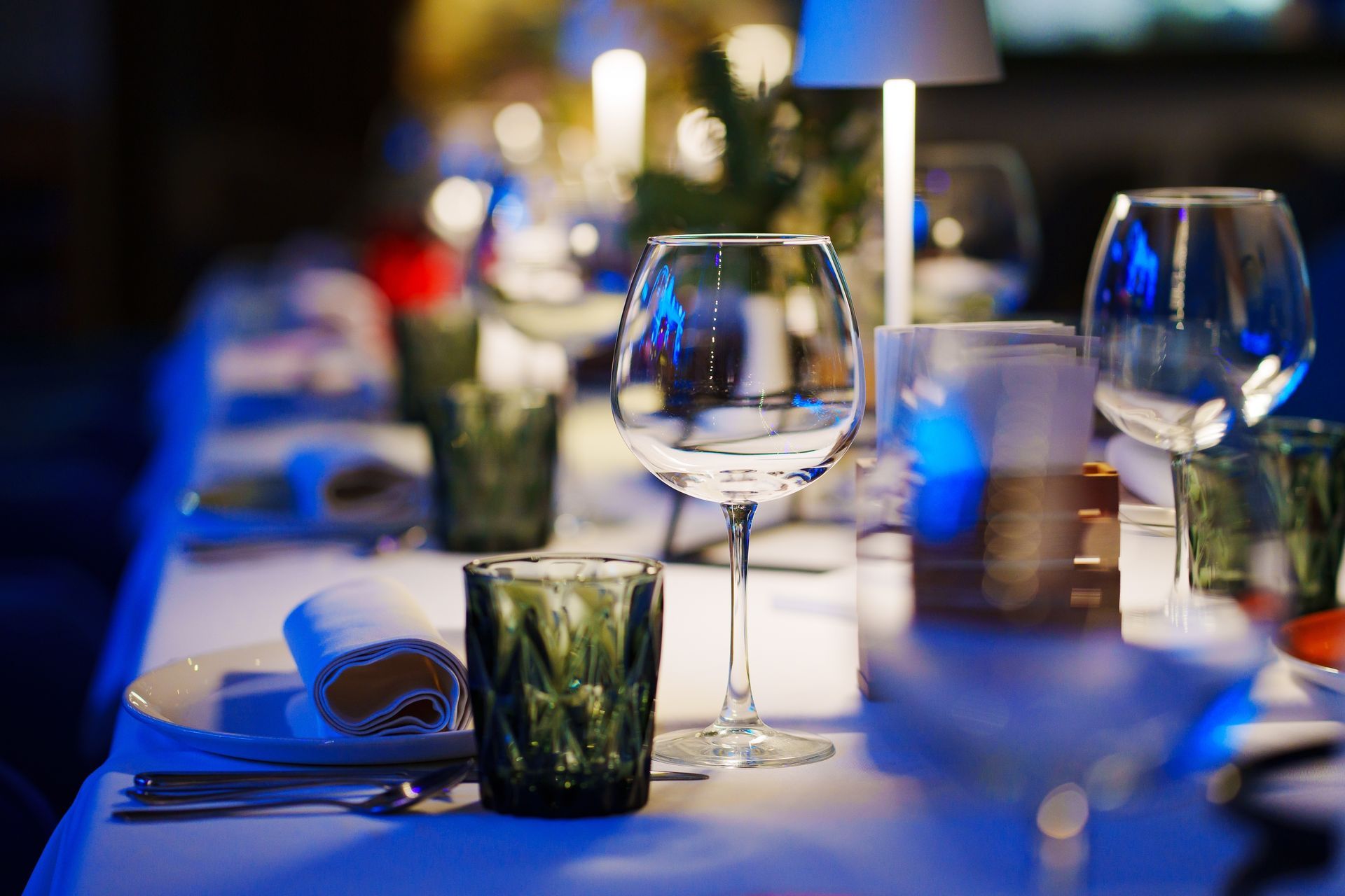 Elegant dinner table set with glassware, candles, and green drinking glasses. Table is white, set in a dimly lit room.