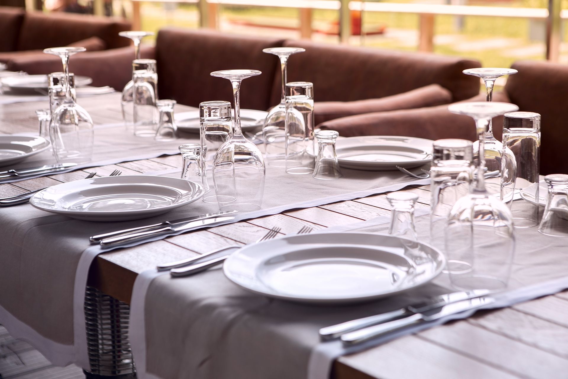 A restaurant table set with plates, glasses, and silverware; ready for guests. The setting is outdoors, with neutral tones.