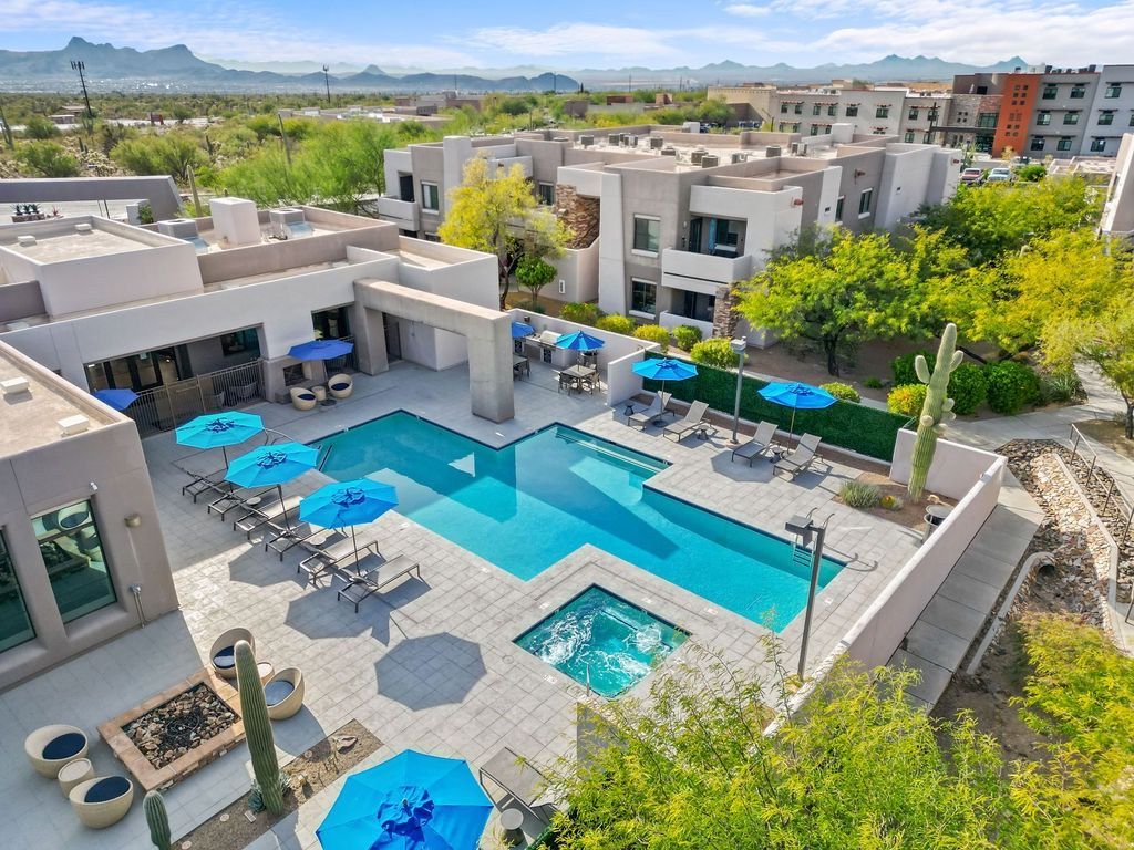Aerial view of a communal pool area with blue umbrellas and lounge chairs at an apartment complex at Legacy Apartments at Dove Mountain in Marana, AZ.