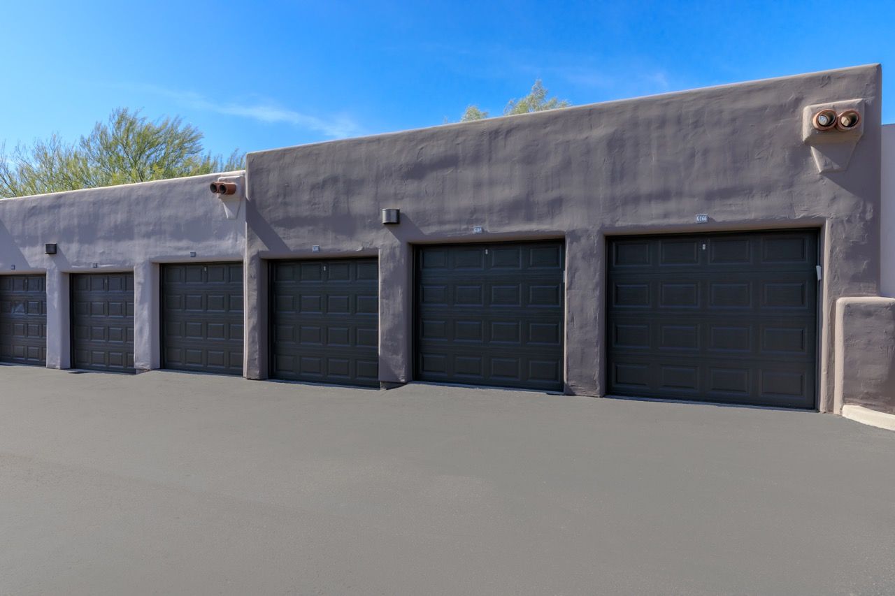 Row of dark gray garage doors along a stucco building under a clear blue sky at Legacy Apartments at Dove Mountain in Marana, AZ.