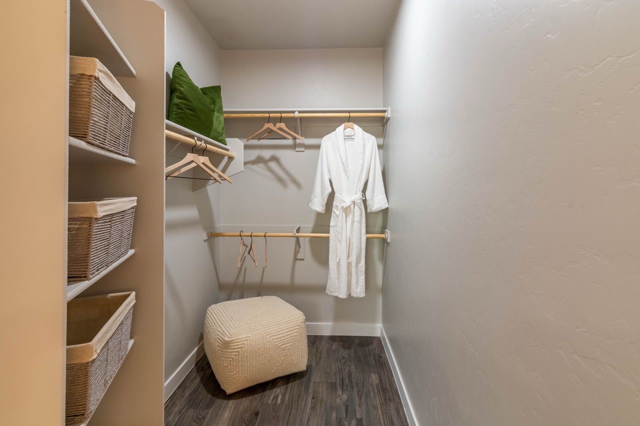 Walk-in closet with shelves, wicker baskets, and a white robe hanging on a rod at Legacy Apartments at Dove Mountain in Marana, AZ.