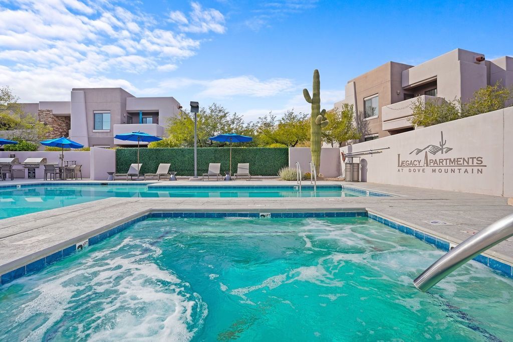 Outdoor apartment community pool with blue umbrellas, lounge chairs, and a cactus sculpture at Legacy Apartments at Dove Mountain in Marana, AZ.