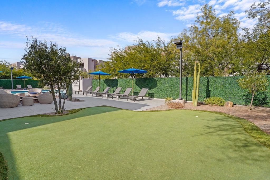 Outdoor community pool area with lounge chairs, blue umbrellas, and a green lawn at Legacy Apartments at Dove Mountain in Marana, AZ.