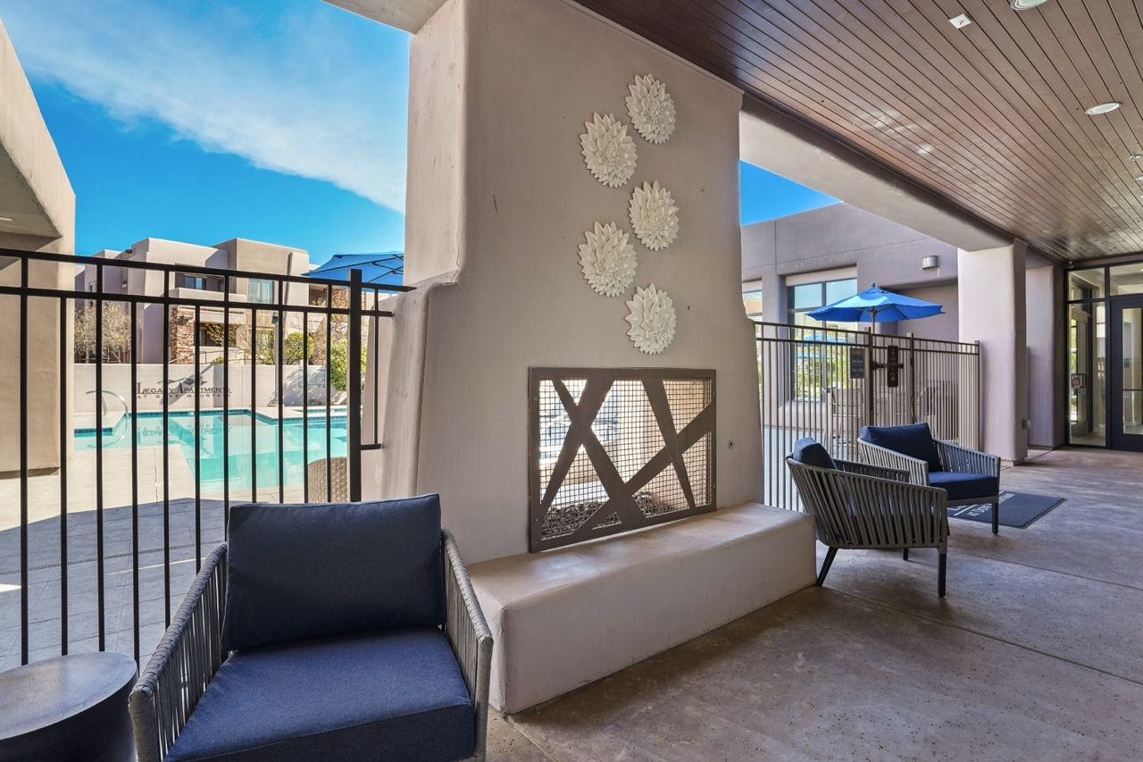Outdoor seating area with a decorative fireplace near a pool under a covered walkway at Legacy Apartments at Dove Mountain in Marana, AZ.